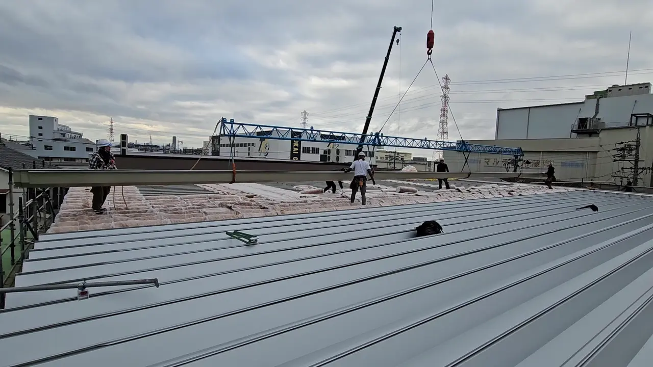 屋根カバー施工動画の一場面。屋根材の吊り上げと屋根上での施工