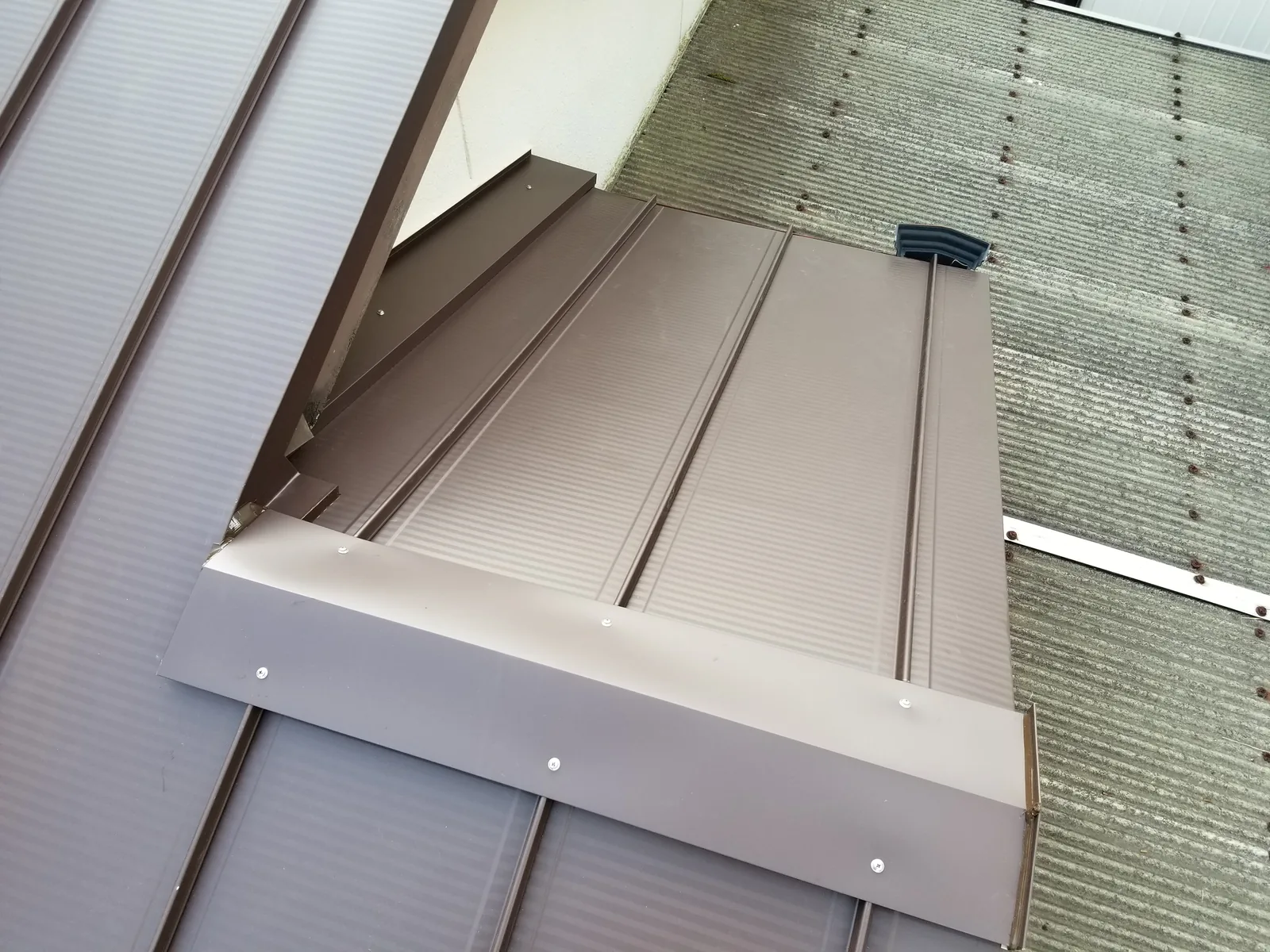 周囲の屋根形状を含めて板金で改修した木造住宅の屋根取り合い部
